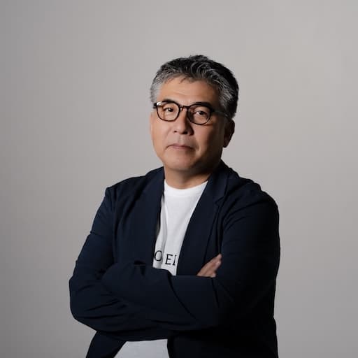 第9研究室　教授　橋本和幸 プロフィール写真1 / 斜めを向き腕を組んでいる。顔は正面を向き真面目な表情をしている。